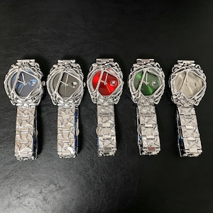 May include: Five unique wristwatches with silver-toned metal bands and intricate, cage-like bezels. Each watch features a different colored face: blue, gray, red, green, and silver. The watch faces have a geometric design.