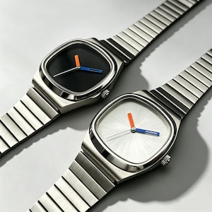 May include: Two stainless steel wristwatches with square faces and matching metal bands. One watch has a black face with orange and blue hands, the other has a white face with orange and blue hands. The watches are displayed on a light gray surface.