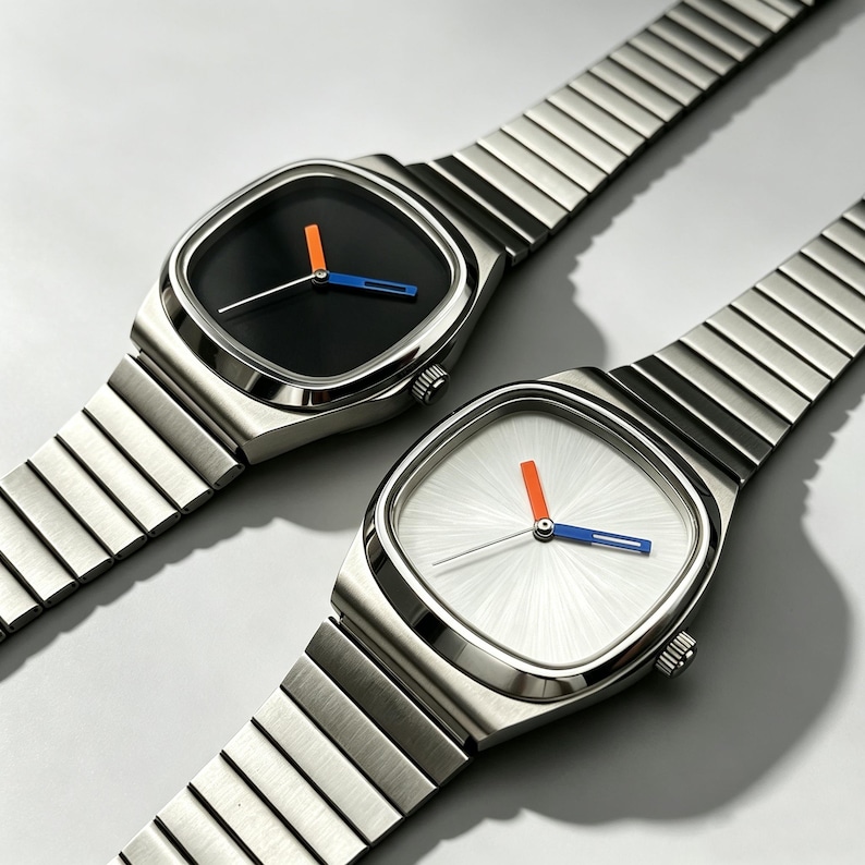 May include: Two stainless steel wristwatches with square faces and matching metal bands. One watch has a black face with orange and blue hands, the other has a white face with orange and blue hands. The watches are displayed on a light gray surface.