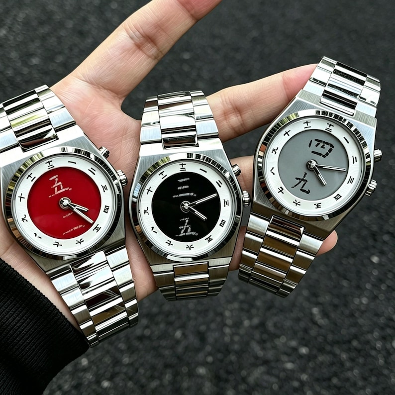 May include: Three stainless steel wristwatches with metallic link bands. Each watch features a white outer dial with black Japanese characters as hour markers. The center dials are red, black, and grey, each displaying distinct Japanese characters.