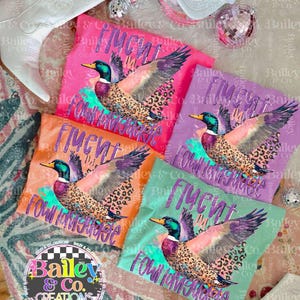 May include: Four colorful t-shirts with a duck graphic and the text "Flyin' In My Four Legged Jeep" printed on them. The shirts are pink, purple, orange, and green.