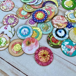 May include: A collection of colorful, round decorative pieces with floral and patterned designs. The pieces feature various colors, including pink, blue, green, and yellow, with intricate details and textures. Some have gold accents.
