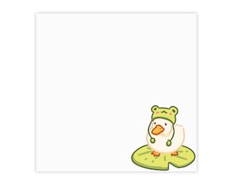 May include: A white square sticker featuring a cartoon duck with an orange beak and feet, wearing a green frog-shaped hat with small ears. The duck is standing on a large, light green lily pad with dark green veins against a plain white background.