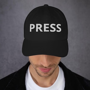 May include: A black baseball cap with a white embroidered "PRESS" on the front.