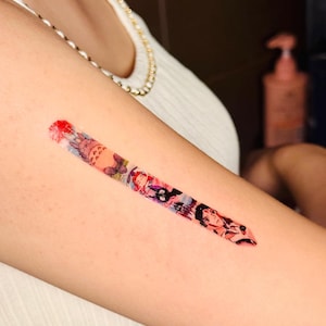 K&ouml;nnte beinhalten: Ein farbenfrohes tempor&auml;res Tattoo auf dem Arm einer Person. Das Tattoo zeigt verschiedene Figuren aus beliebten Anime- und Manga-Serien, darunter Totoro, Kiki liefert aus und Studio Ghibli.