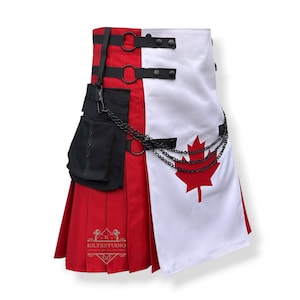 Op de afbeelding: Een rood-witte kilt met een zwarte zak en kettingdetails. De kilt heeft een rood esdoornblad op een wit paneel en de tekst "KILTSSTUDIO" is zichtbaar. De kilt heeft zwarte bandjes en hardware.