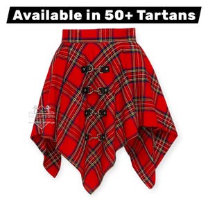 Op de afbeelding: Rode tartan rok met een asymmetrische zoom. De rok heeft een ruitpatroon in rood, geel en blauw. Zwarte leren bandjes met metalen gespen sieren de voorkant. De tekst "Available in 50+ Tartans" staat bovenaan.
