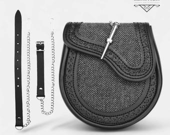 Puede incluir: Un sporran de cuero negro con una cadena plateada y un broche de kilt plateado. El sporran tiene un patrón de espiga y una solapa con costuras decorativas. El sporran es un accesorio tradicional escocés.