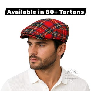 Può includere: Un berretto piatto a quadri rossi, verdi e gialli con corona arrotondata e visiera corta e rigida. Il testo "Available in 80+ Tartans" è visualizzato sopra il berretto e un logo con la scritta "KILTSSTUDIO" è visibile nell'angolo in basso.