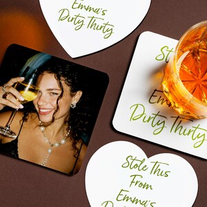 May include: Coasters with green script text reading "Emma's Dirty Thirty". One coaster has a photo of a smiling person with a glass of wine. A glass of amber liquid sits on a coaster, with the text "Stole This From Emma's Dirty Thirty".