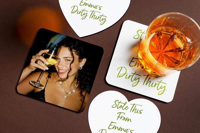May include: Coasters with green script text reading "Emma's Dirty Thirty". One coaster has a photo of a smiling person with a glass of wine. A glass of amber liquid sits on a coaster, with the text "Stole This From Emma's Dirty Thirty".