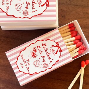 May include: Matchboxes with pink and white striped design. The boxes have red text that reads "Galentine's Girls Day" and "From Elizabeth & Olivia 2026". The matches have red tips.