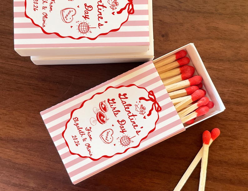 May include: Matchboxes with pink and white striped design. The boxes have red text that reads "Galentine's Girls Day" and "From Elizabeth & Olivia 2026". The matches have red tips.