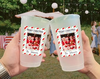 May include: Two frosted plastic cups with a Christmas-themed sticker. The sticker features a family photo, the words "Merry Christmas," and "The Johnsons." The cups are held up in a celebratory gesture.