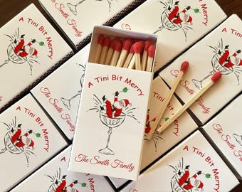 May include: White matchboxes with red-tipped matches. Each box features a cartoon Santa Claus in a cocktail glass, with the text "A Tini Bit Merry" and "The Smith Family" in red.