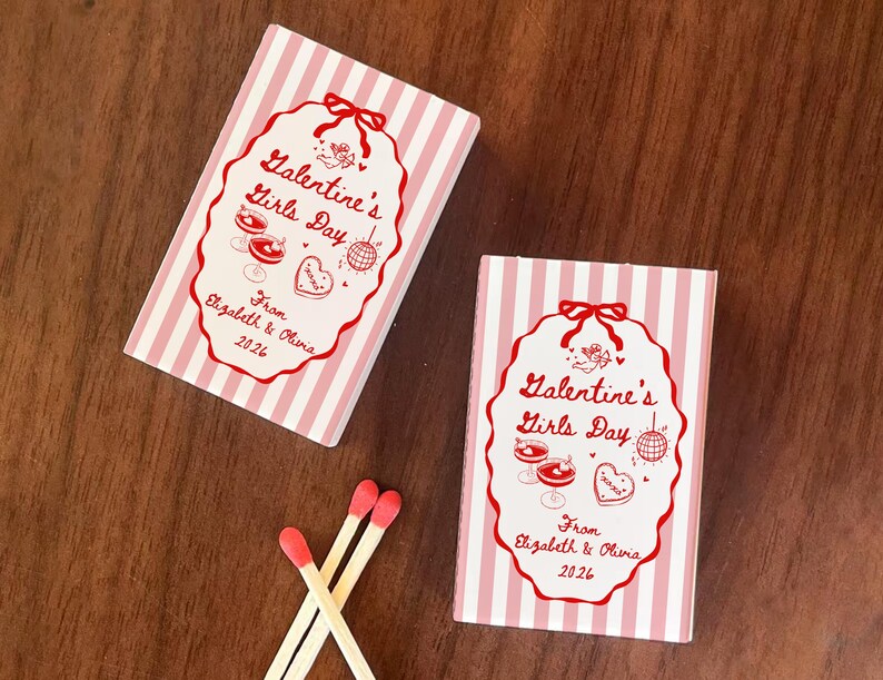 May include: Two matchboxes with pink and white stripes and red text that reads "Galentine's Girls Day" and "From Elizabeth & Olivia 2026". Three matches with red tips are also visible.