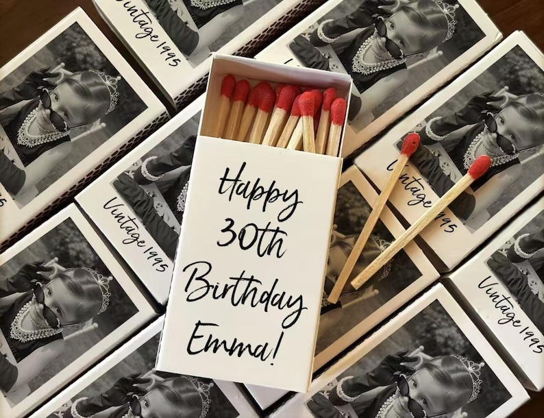 Op de afbeelding: Een witte luciferdoos met de tekst "Happy 30th Birthday Emma!" en meerdere dozen met een zwart-wit foto en de tekst "Vintage 1995". De luciferkoppen zijn rood.