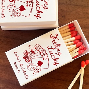 May include: White matchboxes with red text that reads "Feeling Lucky" and "Sophia's Bachelorette, Miami, FL." The boxes feature playing card and dice graphics. The matches have red tips.