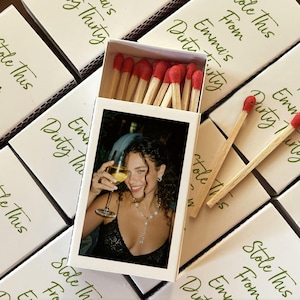 May include: Matchboxes with red-tipped matches. The boxes are white with green text that reads "Stole This From Emma's Dirty Thirty." One box is open, revealing a photo of a woman holding a glass of wine.