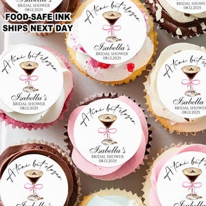 May include: An overhead shot of cupcakes with decorative toppers. Each topper features a cocktail illustration with the text "Atini bit closer" and "Isabella's BRIDAL SHOWER 08.12.2025". The cupcakes have various frosting colors.