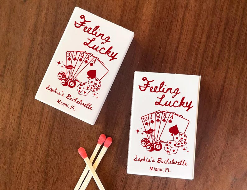 May include: Two white matchboxes with red text that reads "Feeling Lucky" and "Sophia's Bachelorette, Miami, FL." The boxes feature a poker-themed design with playing cards, dice, and cherries. Three matches with red tips are also visible.