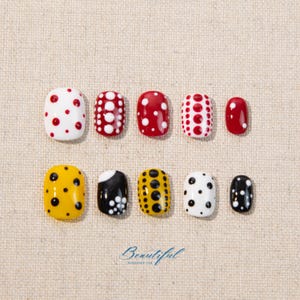 May include: A collection of ten artificial nails with various designs. The nails feature a mix of colors, including white, red, yellow, and black, adorned with polka dots and floral patterns. The word "Beautiful" is written in cursive at the bottom.
