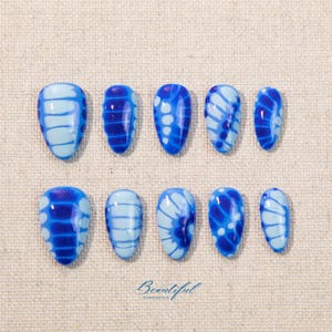 May include: A set of ten blue and light blue press-on nails. Each nail features a unique design with stripes, dots, and swirls. The word "Beautiful" is written in cursive at the bottom.