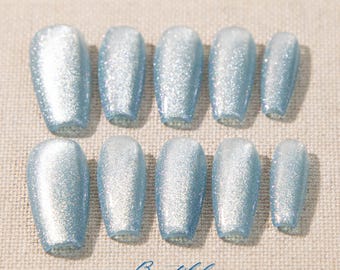 Könnte beinhalten: Ein Satz von zehn hellblauen, glitzerbedeckten Kunstnägeln. Die Nägel haben eine Sargform mit abgerundeter Spitze. Das Wort "Beautiful" ist in Schreibschrift am unteren Rand des Bildes geschrieben.