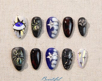 May include: A set of ten almond-shaped artificial nails with various designs. The designs include an eye, spiders, stars, and abstract patterns in colors like black, blue, white, and iridescent hues. The word "Beautiful" is written in cursive at the bottom.