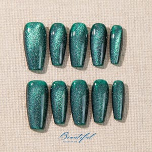 May include: A set of ten emerald green press-on nails with a glittery finish. The nails are in various sizes and shapes, with a rectangular form. The word "Beautiful" is written in cursive at the bottom.