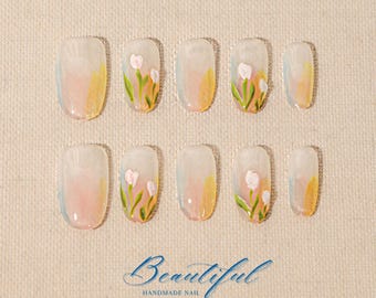 Könnte beinhalten: Ein Set aus zehn künstlichen Nägeln mit floralem Design. Jeder Nagel hat einen Farbverlauf aus Pastellfarben und handgemalte weiße Blumen mit grünen Stielen und Blättern. Der Text "Beautiful Handmade Nail" befindet sich unten.