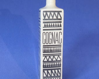 May include: A rectangular white bottle with a narrow neck, featuring black geometric patterns and the word "COGNAC" in bold letters. The bottle has a minimalist design, suitable for spirits.