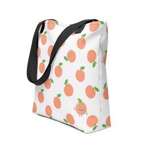 May include: White tote bag with a repeating pattern of cartoon peaches in shades of orange and green. The bag has black straps and a white background. The peaches have green leaves and some have smiling faces.