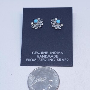 May include: A pair of sterling silver flower-shaped stud earrings with a turquoise center stone. The earrings are displayed on a black card with the text "GENUINE INDIAN HANDMADE FROM STERLING SILVER". A quarter is included for size reference.