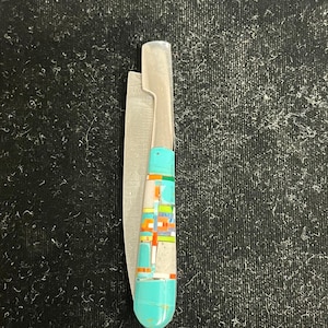 May include: A silver pocket knife with a turquoise, orange, white and green inlay handle.