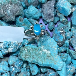 May include: A silver ring with a turquoise stone in an oval shape. The ring is surrounded by turquoise stones of various sizes and shades of blue and green.