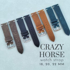 Op de afbeelding: Een verzameling Crazy Horse horlogebandjes in verschillende kleuren, waaronder bruin, zwart en blauw. Elke band heeft een zilveren gesp en witte stiksels. De bandjes zijn verkrijgbaar in breedtes van 18, 20 en 22 mm.