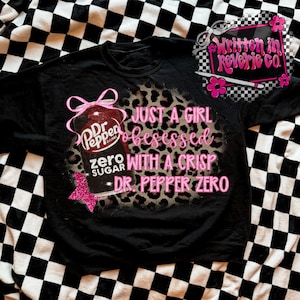 Könnte beinhalten: Schwarzes Sweatshirt mit einem Dr. Pepper Zero-Motiv. Das Design zeigt eine Dr. Pepper-Flasche mit einer rosa Schleife, einem rosa Stern und dem Text "JUST A GIRL obsessed WITH A CRISP DR. PEPPER ZERO."