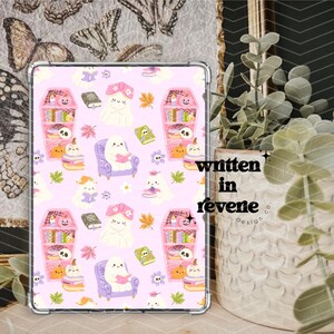 Puede incluir: Una funda rosa para tableta con un patrón repetido de fantasmas, calabazas, libros y estanterías con forma de ataúd. El diseño incluye hojas de otoño y flores. El texto "written in revene design co" es visible.