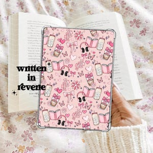 Pode incluir: Capa para iPad rosa e branca com um design de livros, xícaras de café, borboletas, laços e fones de ouvido. A capa é feita de um material transparente com um design impresso.