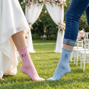 Puede incluir: Un par de calcetines personalizados, uno rosa y otro azul claro, con volantes y iniciales bordadas. El calcet&iacute;n rosa tiene "EJ" bordado en rosa m&aacute;s oscuro, y el calcet&iacute;n azul tiene "FS" bordado en azul m&aacute;s oscuro. Los calcetines est&aacute;n sobre un c&eacute;sped verde.