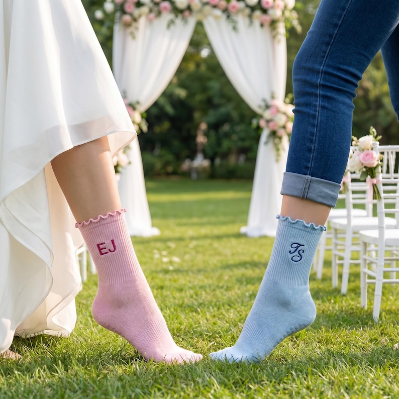 Puede incluir: Un par de calcetines personalizados, uno rosa y otro azul claro, con volantes y iniciales bordadas. El calcet&iacute;n rosa tiene "EJ" bordado en rosa m&aacute;s oscuro, y el calcet&iacute;n azul tiene "FS" bordado en azul m&aacute;s oscuro. Los calcetines est&aacute;n sobre un c&eacute;sped verde.