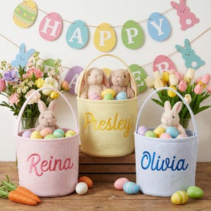 Könnte beinhalten: Drei pastellfarbene Osterkörbe mit Plüschhasen und bunten Eiern. Die Körbe sind mit den Namen Reina, Presley und Olivia personalisiert. Ein Banner darüber zeigt "HAPPY".