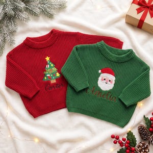 May include: A red knit sweater featuring an embroidered Christmas tree and the name Carter, and a green knit sweater featuring an embroidered Santa Claus face and the name Amelia, both with long sleeves and ribbed crew necklines.