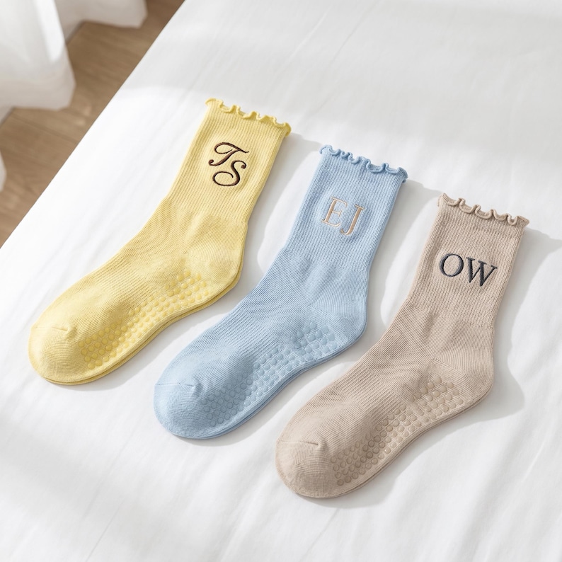 Puede incluir: Tres pares de calcetines personalizados en colores pastel: amarillo, azul claro y beige. Cada calcet&iacute;n presenta una inicial bordada diferente en un color contrastante. Los calcetines tienen un borde superior con volantes y una suela texturizada.