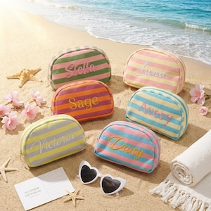 May include: A collection of colorful, striped cosmetic bags with embroidered names: Stella, Luna, Sage, Avery, Victoria, and Daisy. The bags are arranged on a sandy beach with sunglasses, a towel, and starfish.