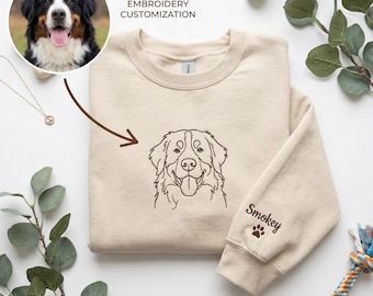 May include: A beige crewneck sweatshirt featuring a brown embroidered line art portrait of a Bernese Mountain Dog on the chest. The sleeve is embroidered with the name Smokey and a small paw print. Text above reads PHOTO TO LINE EMBROIDERY CUSTOMIZATION.