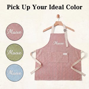 May include: A red and white striped apron with the name "Maeve" embroidered in white. The apron has a pocket and is hanging on a wooden hanger. The image also shows three circles with the name "Maeve" embroidered on different colored striped backgrounds.
