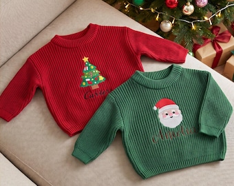 May include: A red ribbed knit jumper featuring an embroidered Christmas tree and the name Carter, alongside a green ribbed knit jumper featuring an embroidered Santa Claus face and the name Amelia, both with long sleeves and crew necklines.