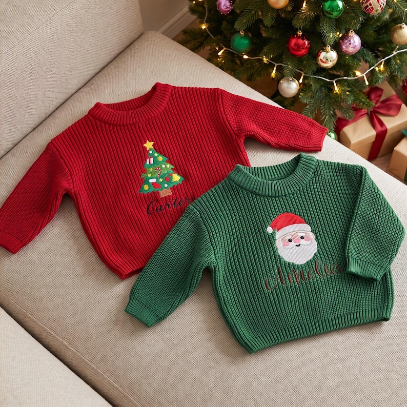 May include: A red ribbed knit sweater featuring an embroidered Christmas tree and the name Carter, alongside a green ribbed knit sweater featuring an embroidered Santa Claus face and the name Amelia, both with long sleeves and crew necklines.